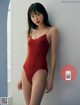 A woman in a red bodysuit leaning against a wall.