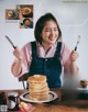 A woman holding a knife and fork in front of a stack of pancakes.