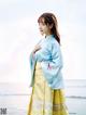 A woman in a blue and yellow hanbok standing on the beach.